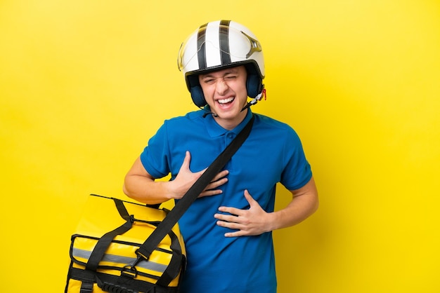 Jovem brasileiro com mochila térmica isolada em fundo amarelo sorrindo muito