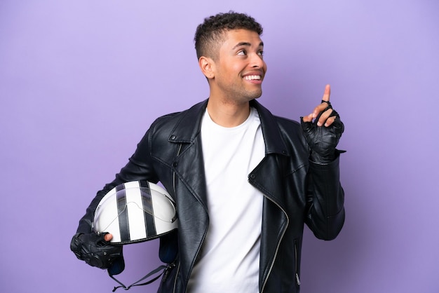 Jovem brasileiro com um capacete de moto isolado em fundo roxo apontando uma ótima ideia