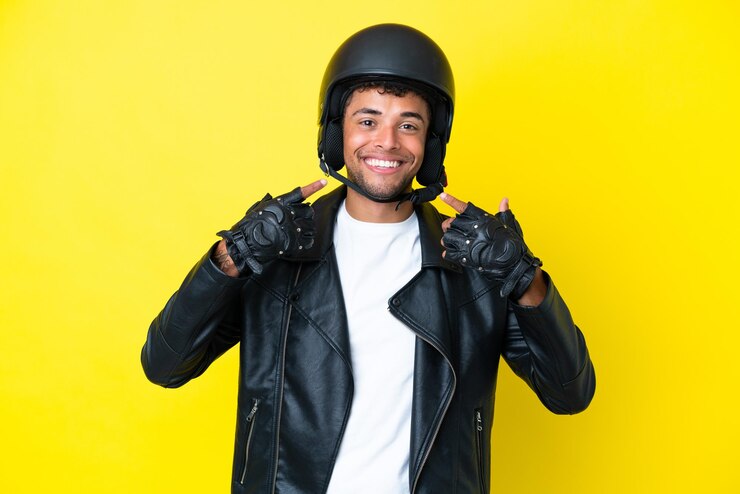 Foto jovem brasileiro com um capacete de motociclista isolado em um fundo amarelo fazendo um gesto de polegar para cima
