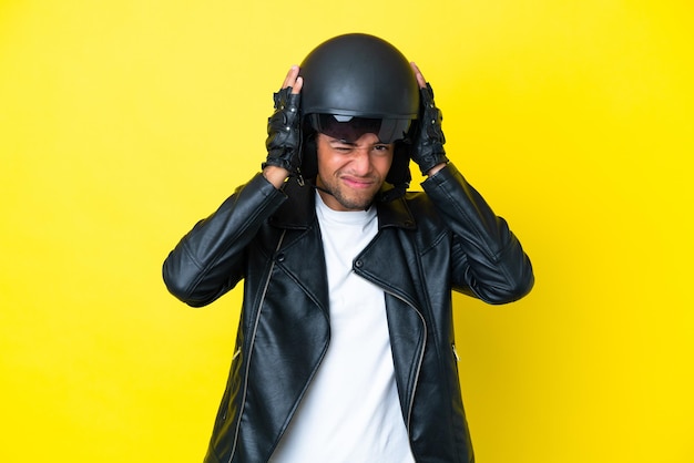 Jovem brasileiro com um capacete de motociclista isolado em um fundo amarelo frustrado e cobrindo as orelhas