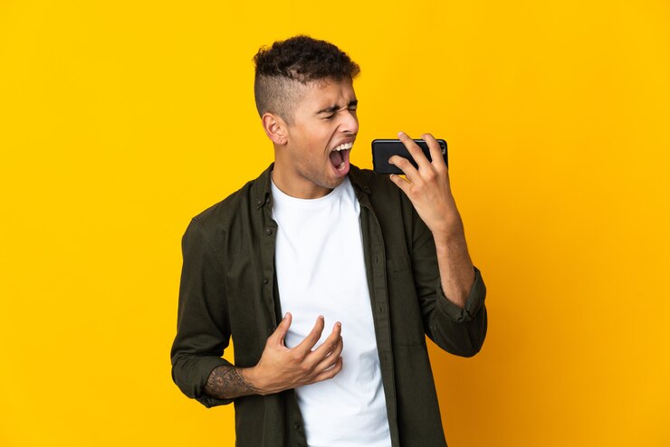 Foto jovem brasileiro em uma parede isolada usando celular e cantando