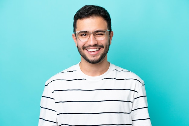 Jovem brasileiro isolado em fundo azul com óculos e expressão feliz