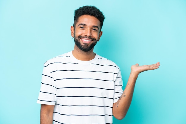 Jovem brasileiro isolado em fundo azul segurando copyspace imaginário na palma da mão para inserir um anúncio