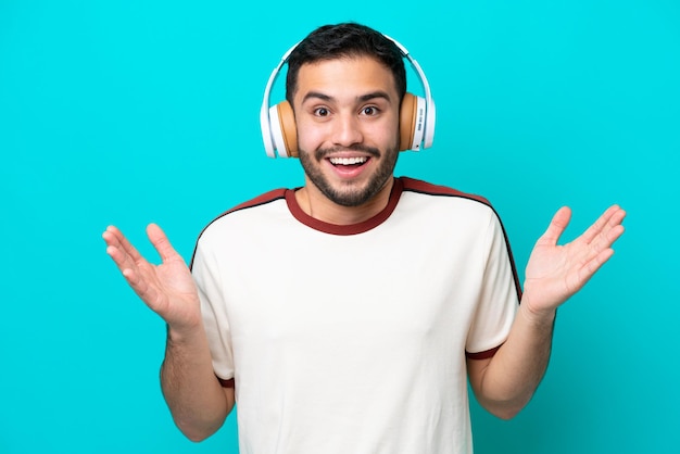 Jovem brasileiro isolado em fundo azul surpreso e ouvindo música