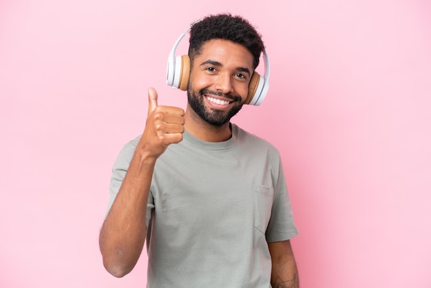 Jovem brasileiro isolado em fundo rosa ouvindo música e com o polegar para cima