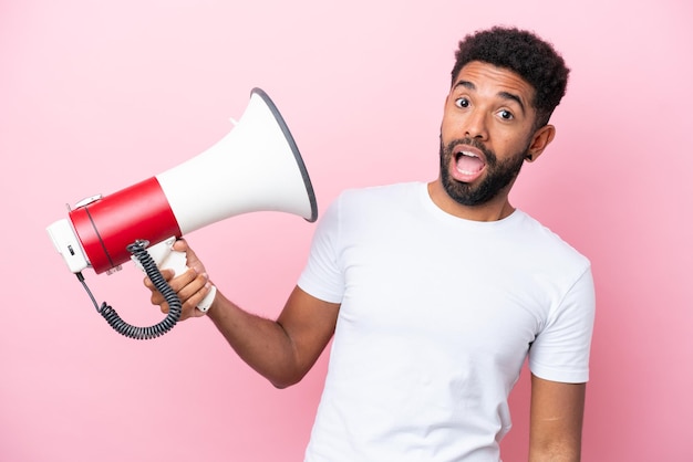 Jovem brasileiro isolado em fundo rosa segurando um megafone com expressão estressada