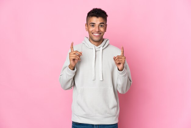 Jovem brasileiro isolado em um fundo rosa apontando uma ótima ideia