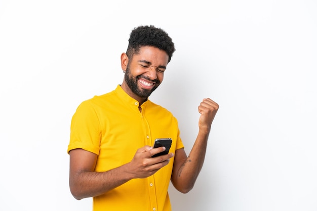 Jovem brasileiro isolado no fundo branco com o telefone em posição de vitória