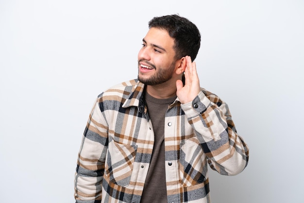 Jovem brasileiro isolado no fundo branco ouvindo algo colocando a mão na orelha