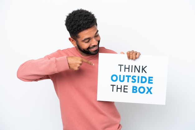 Jovem brasileiro isolado no fundo branco segurando um cartaz com texto Think Outside The Box e apontando-o