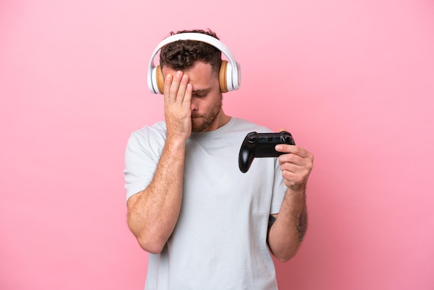 Jovem brasileiro jogando com controlador de videogame isolado em fundo rosa com expressão cansada e doente