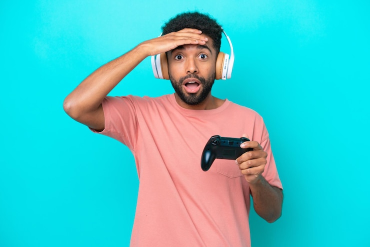 Foto jovem brasileiro jogando com um controlador de videogame isolado em fundo azul com expressão de surpresa