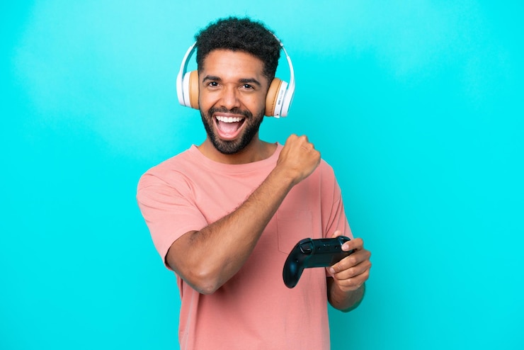 Foto jovem brasileiro jogando com um controlador de videogame isolado em fundo azul comemorando uma vitória