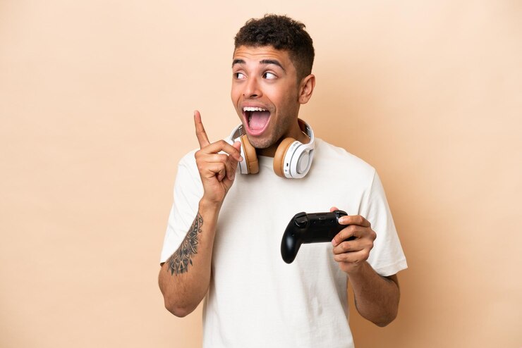 Foto jovem brasileiro jogando com um controlador de videogame isolado em fundo bege com a intenção de perceber a solução enquanto levanta um dedo