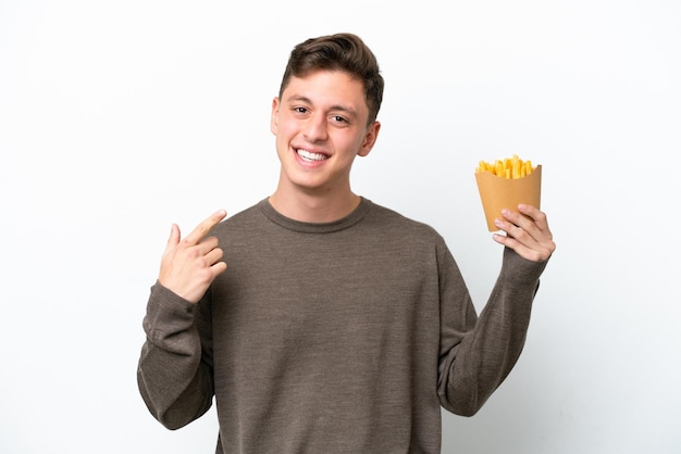 Jovem brasileiro segurando batatas fritas isoladas no fundo branco, dando um polegar para cima gesto