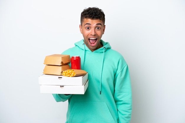 Jovem brasileiro segurando fast food isolado no fundo branco com expressão facial de surpresa