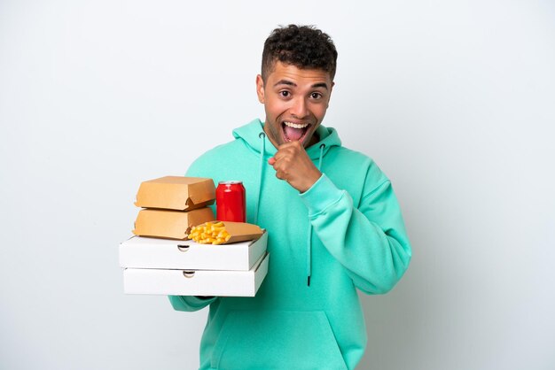 Jovem brasileiro segurando fast food isolado no fundo branco comemorando uma vitória