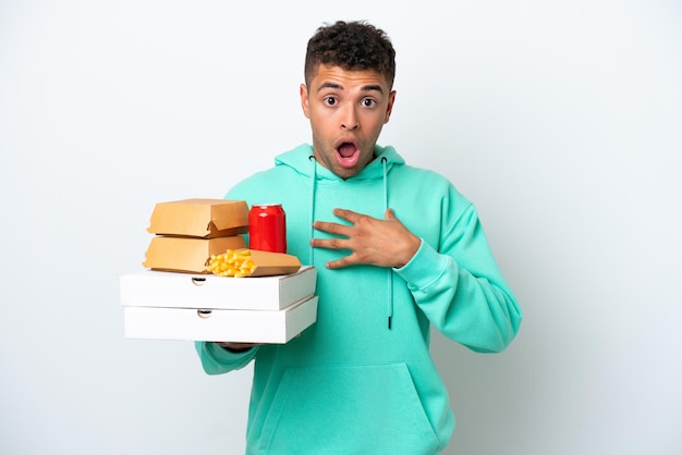 Jovem brasileiro segurando fast food isolado no fundo branco surpreso e chocado ao olhar para a direita