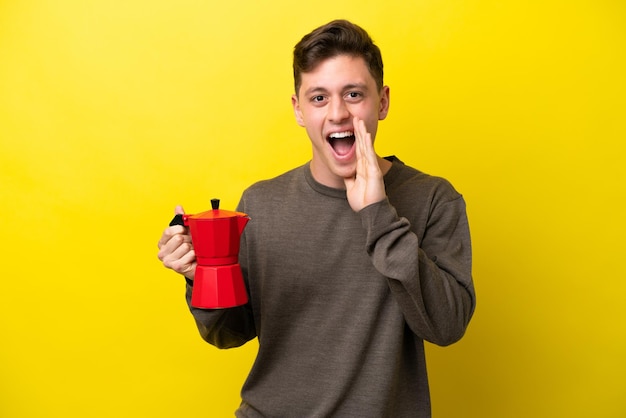 Jovem brasileiro segurando o bule de café isolado em fundo amarelo com surpresa e expressão facial chocada