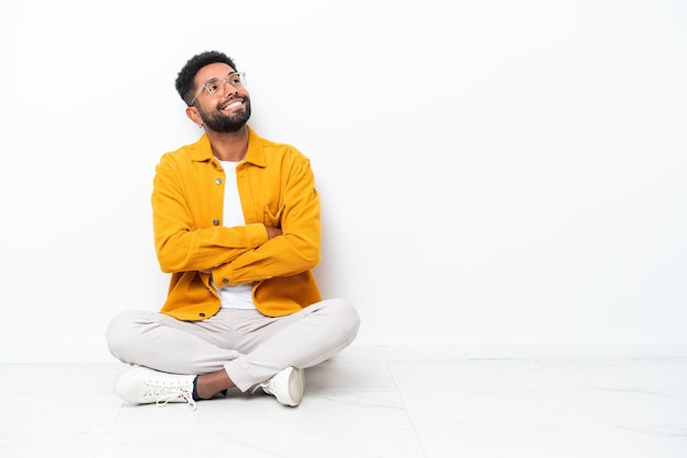 Jovem brasileiro sentado no chão isolado no fundo branco olhando para cima enquanto sorria