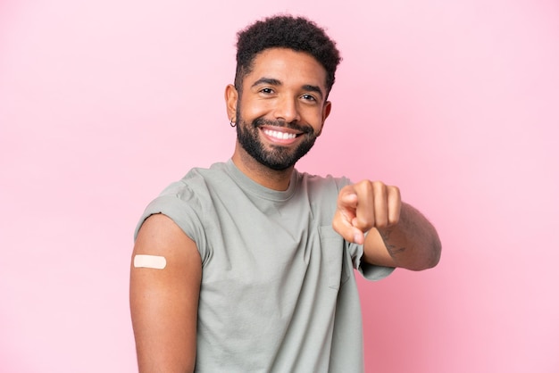 Foto jovem brasileiro usando um curativo isolado no fundo rosa aponta o dedo para você com uma expressão confiante