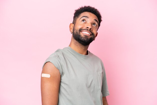 Foto jovem brasileiro usando um curativo isolado no fundo rosa olhando para cima enquanto sorria