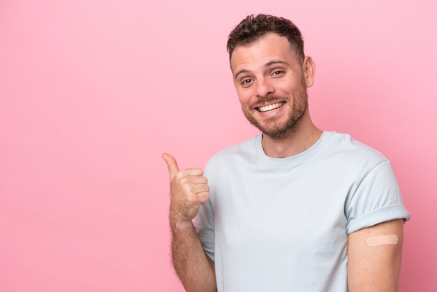 Jovem brasileiro vestindo um curativo isolado no fundo rosa, apontando para o lado para apresentar um produto