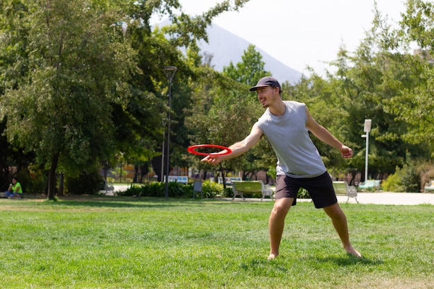 Jovem brincando com frisbee em um dia ensolarado no parque. Conceitos de recreação de atividades esportivas