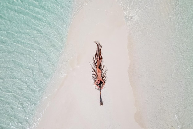 Jovem bronzeada tomando banho de sol na folha de palmeira mulher vestindo biquíni na praia em uma areia branca de cima vista do drone