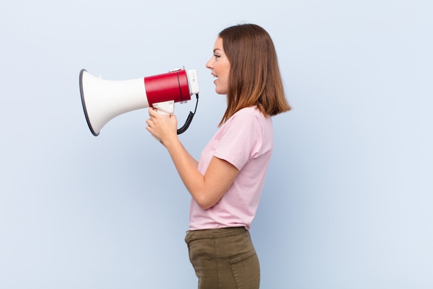 Jovem cabeça vermelha mulher contra uma parede plana com um megafone