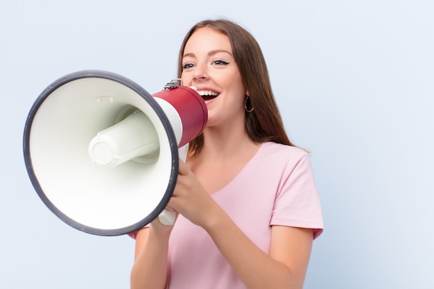 Jovem cabeça vermelha mulher contra uma parede plana com um megafone