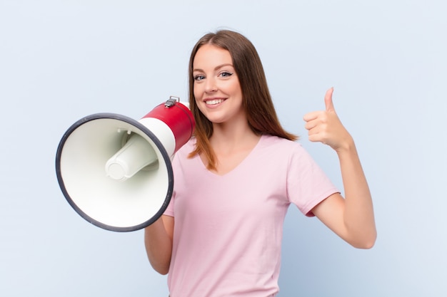 Jovem cabeça vermelha mulher contra uma parede plana com um megafone