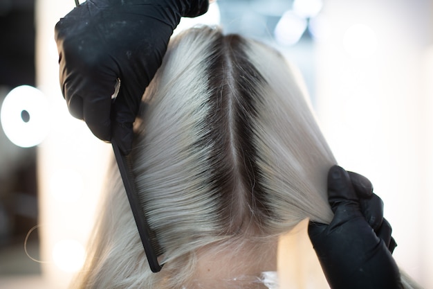 Jovem cabeleireira tingir o cabelo no salão de beleza. Coloração profissional de raízes de cabelo