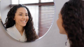Foto jovem calma atraente em roupão de banho no banheiro parece no reflexo do espelho desfrutar de uma pele saudável