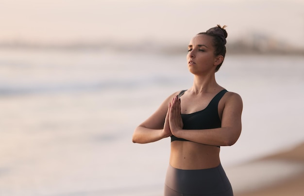 Jovem calma meditando na areia da praia durante a sessão de ioga