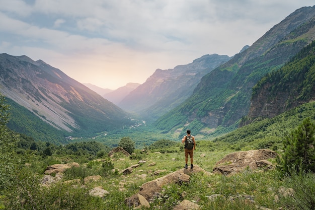 Jovem caminhando no topo de uma montanha verde durante o pôr do sol