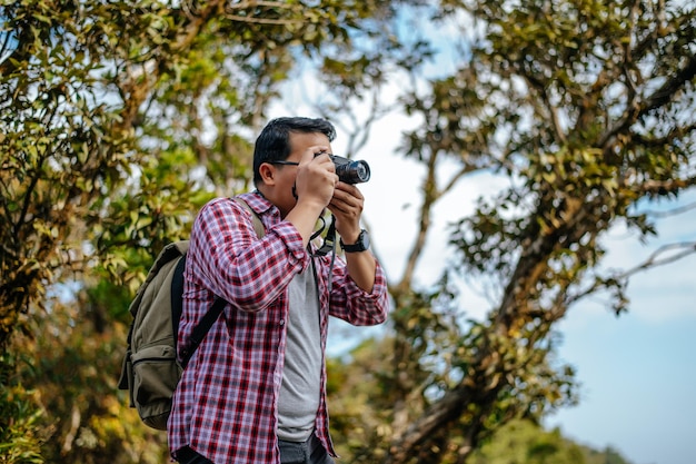 Jovem caminhante asiático e mochila usam câmera para tirar fotos no espaço de cópia da floresta