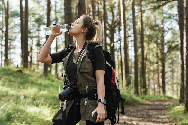 Jovem caminhante bebendo água de uma garrafa reutilizável em uma floresta verde
