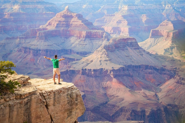 Jovem caminhante está de pé em um penhasco íngreme admirando a vista incrível sobre o famoso Grand Canyon em um belo dia ensolarado com céu azul no verão Grand Canyon National Park Arizona EUA