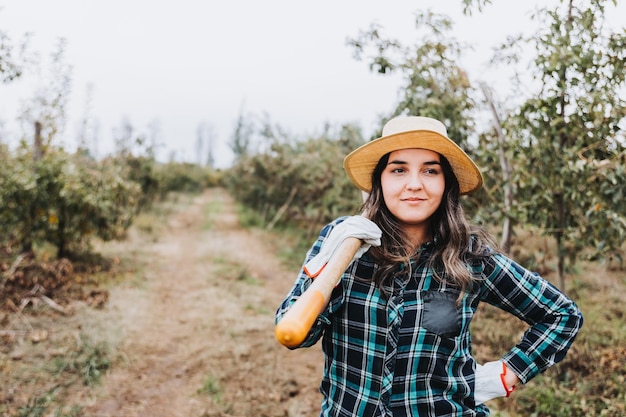 Jovem camponesa latina sorridente com uma pá no ombro Papel das mulheres na agricultura