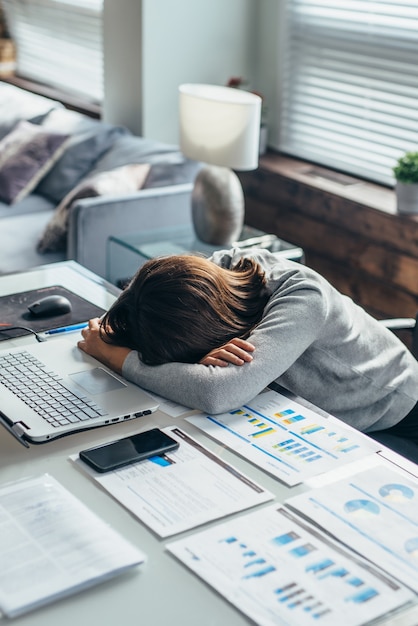 Jovem cansada dorme no trabalho com a cabeça sobre a mesa.