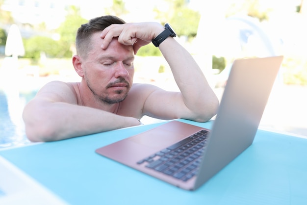 Jovem cansado com os olhos fechados em frente a um laptop na piscina