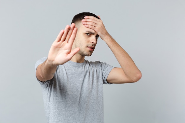 Jovem cansado em roupas casuais, colocando a mão na testa, mostrando o gesto de parar com a palma da mão