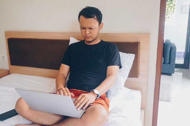 Jovem cansado verificando seu laptop enquanto está sentado na cama