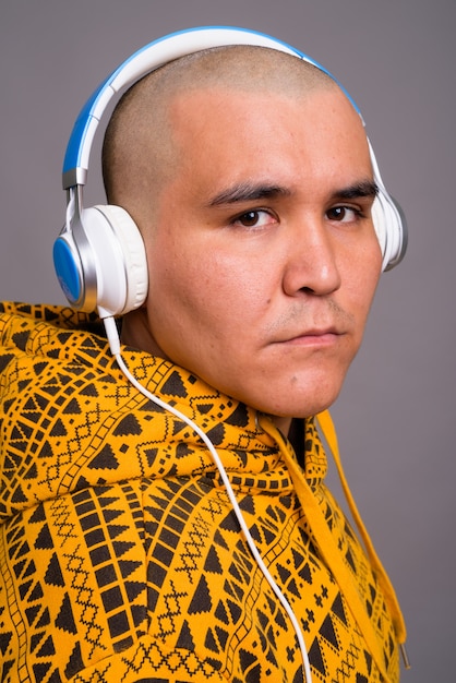 Foto jovem careca asiática ouvindo música contra parede cinza