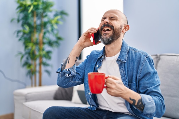 Jovem careca falando em smartphone tomando café em casa