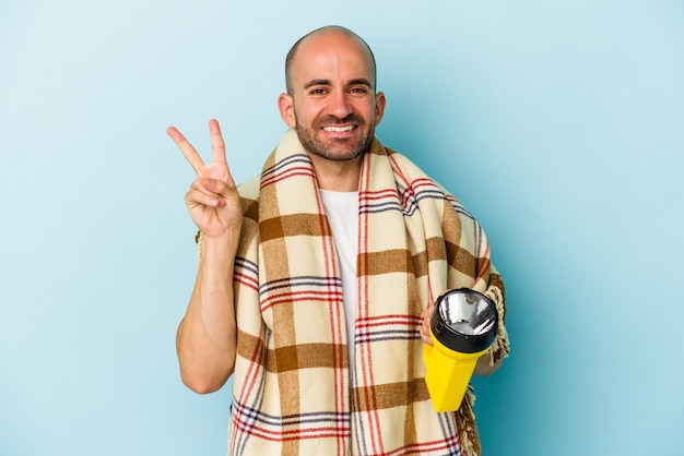 Jovem careca segurando lanterna vintage isolada em fundo azul alegre e despreocupada, mostrando um símbolo de paz com os dedos.