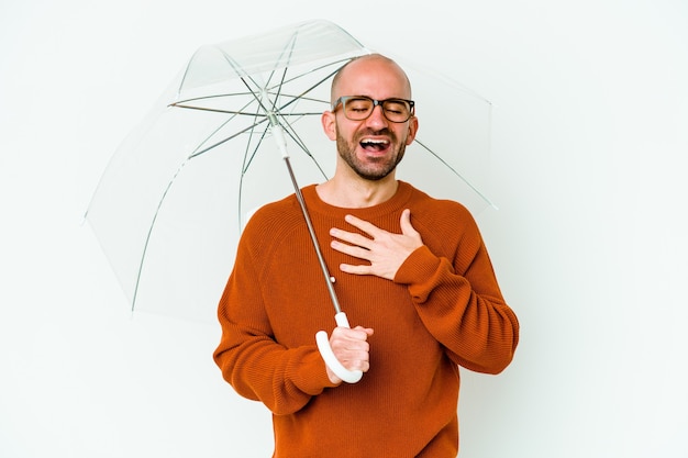 Jovem careca segurando um guarda-chuva isolado e rindo alto mantendo a mão no peito