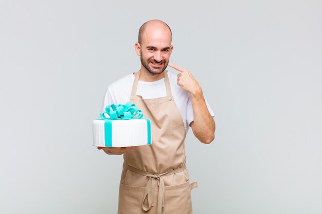 Jovem careca sorrindo com confiança apontando para o próprio sorriso largo, atitude positiva, relaxada e satisfeita