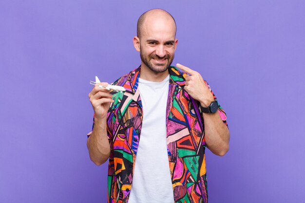 Jovem careca sorrindo com confiança apontando para o próprio sorriso largo